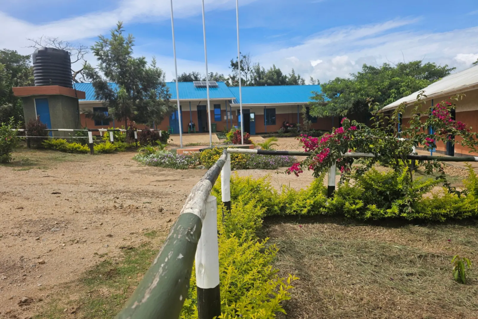 Classroom blocks, a water tower and three flagpoles on the Spectrum Secondary School campus, with bougainvillea and hedges in the foreground.